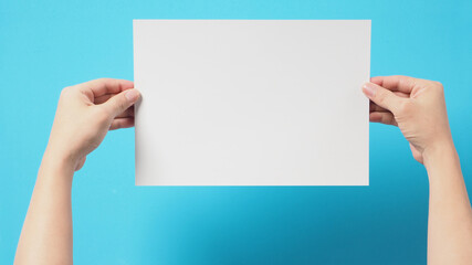 Obraz premium The hand is holding the white A4 paper on blue background.