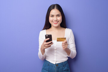 Portrait of Young Asian woman is using cell phone with credit card on purple background
