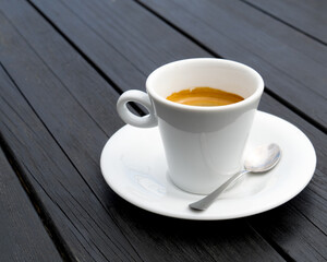 White cup with hot coffee on a black wooden table.