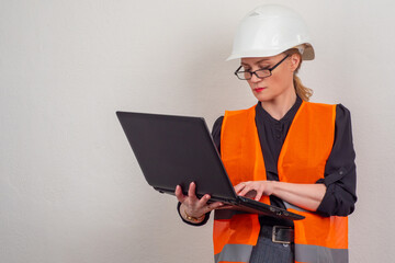 Girl works as an engineer at the enterprise. Female engineer with a laptop in her hands. Young woman works in a box office and vest. Girl in protective uniform. Engineer stands with laptop