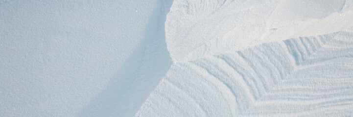 Obraz premium Beautiful winter background with snowy ground. Natural snow texture. Wind sculpted patterns on snow surface. Wide panoramic texture for background and design.
