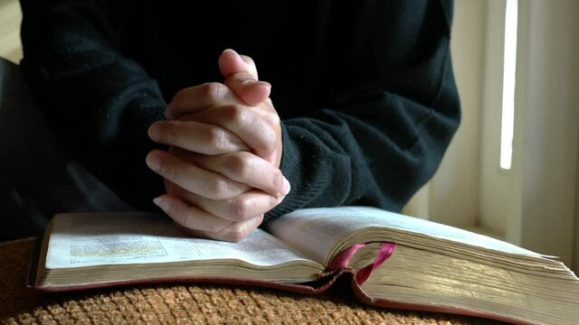 Woman with hands crosses on top of bible in prayer posture. Closeup view.