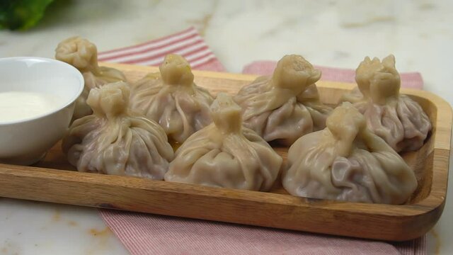 Close-up of delicious khinkali, dumplings poured with melted butter. Khinkali on a wooden plate with sour cream. Khinkali on a marble background.