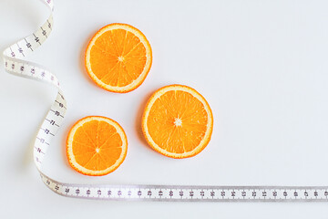 Orange fruit slices with measuring tape isolated on white background. Diet for lose weight, still life background. Healthy lifestyle concept