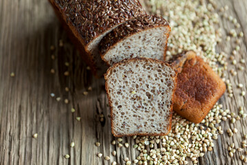 Bread made from organic green buckwheat with the addition of flaxseed. A loaf and sliced slices on an old wooden table next to a groats