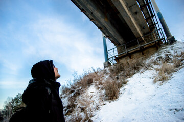 Man in dark clothes and glasses look up at the old bridge
