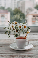 a bouquet of daisies and tea on a white wooden table