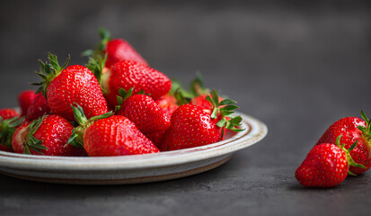 Ripe strawberries in plate on dark background with copy space