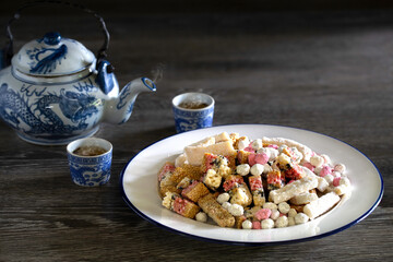 Chinese snack in white dish and Chinese tea in cup and pot on old brown wooden table in dim light