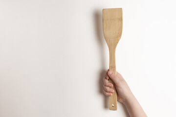 .A natural bamboo spatula in a child’s hand is a view of a surga, on a white background. Little cook with a bamboo spatula.