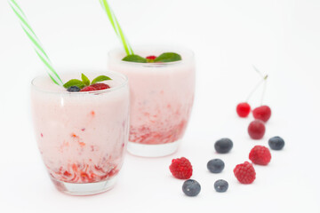 Berries smoothies in two glasses with straws on white background. Fresh homemade smoothie with blueberries, raspberries and sour cherries.
