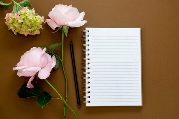 Open note book with flowers - roses, hydrangea. Brown background. Flat lay.