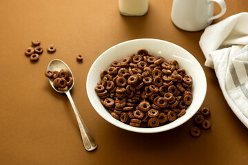 Chocolate cereal rings in bowl brown background. Breakfast for kind.