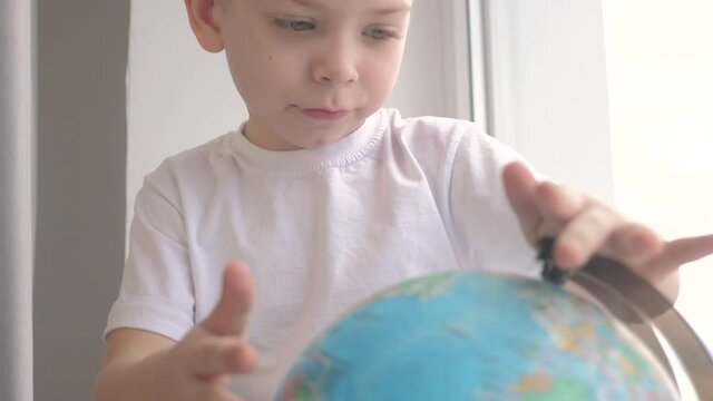 lifestyle boy studies globe. education travel tourism concept. child twists the globe sits on a window sill. kid looking for a country on a globe map. world map geography study