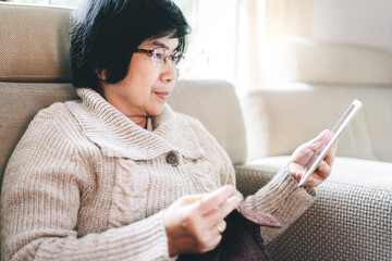 Asian elderly woman wear sweater knitting yarn with tablet for study online.
