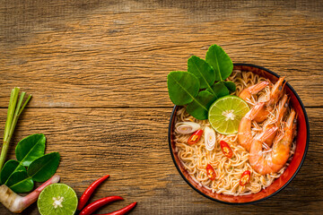 Thai style noodle in bowl, Tom Yum Kung with Thai herbs, chili, galangal, lime, lemongrass and kaffir lime leaf on wooden background.