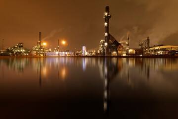 Fototapeta na wymiar Refineries reflection and its chimney during the on fire sunset golden hour moment at Rotterdam, Netherlands