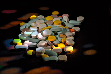 White, yellow, red, orange and blue pills on a black cardboard background. Medication on a dark background with contrasting dramatic light.