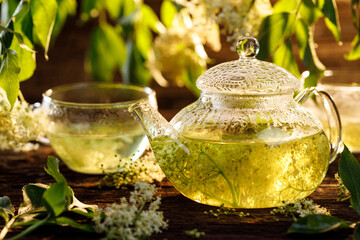 Elderflower tea infusion of elder white flowers in a glass teapot on a wooden table. Healthy and...