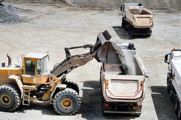 wheel loader with scoop working on construction site and loading gravel on dumper trucks. Heavy...