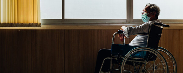 Retirement concept. Panoramic asian elderly man wear mask sitting in wheelchair while looking out...
