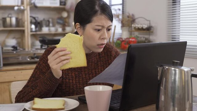 korean woman eating toast is astonished with anger while checking on telephone bill. asian housekeeper having headache finding out charge go up steeply as her son made too many phone calls