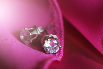 Silver diamond earrings on pink fabric