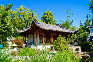 Scenic view of a beautiful Chinese temple building in the Chinese Garden in the city of Stuttgart, Germany under a clear blue sky. Bushes and plants surround this peaceful spot.