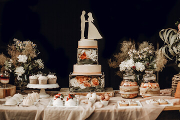 Candy bar. White wedding cake decorated by flowers standing of festive table with deserts, strawberry tartlet and cupcakes. Wedding. Reception Tartlets
