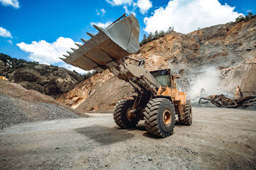 Industrial wheel loader working on construction site, loading and transporting gravel into dumper...
