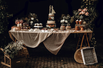 Candy bar. White wedding cake decorated by flowers standing of festive table with deserts, strawberry tartlet and cupcakes. Wedding. Reception Tartlets