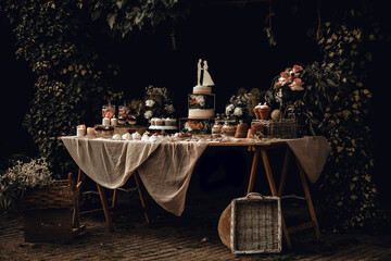 Candy bar. White wedding cake decorated by flowers standing of festive table with deserts, strawberry tartlet and cupcakes. Wedding. Reception Tartlets
