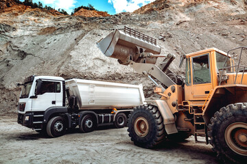 Wheel loader bulldozer with blade loading dumper trucks on construction site. Excavator details