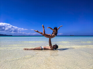 Fototapeta na wymiar A guy with a girl of European appearance do complex tricks and pair acrobatics on the beach
