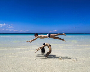 Fototapeta na wymiar A guy with a girl of European appearance do complex tricks and pair acrobatics on the beach