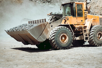 Large wheel loader on quarry site transporting and loading gravel into dumper trucks