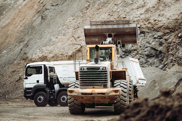 Fototapeta na wymiar Industrial dumper trucks and wheel loader working on construction site, loading and unloading gravel and earth. heavy duty machinery activity.