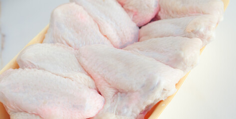 Chilled chicken wings in a yellow tray, fresh meat from the store on a white table. High protein in chicken