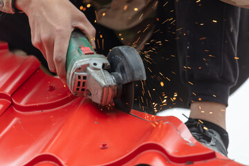 A worker cuts a red metal roof tile.