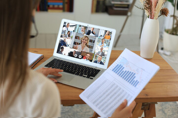 Business woman in headphones talking to her colleagues in video conference. Multiethnic business team working from home using laptop, discussing financial report of their company.