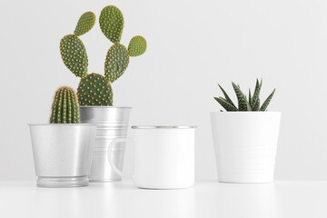 Enamel mug mockup with various types of cactus and a succulent plant on a white table.