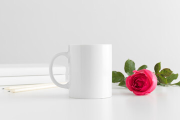 Mug mockup with books and a pink rose on a white table.