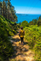 Obraz premium A young brunette on the trail trekking down to the town of Orio, Guipuzcoa, Basque Country. Excursion from San Sebastián to the town of Orio through Mount Igeldo walking 3 friends.