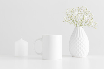 Mug mockup with a candle and a gypsophila on a white table.