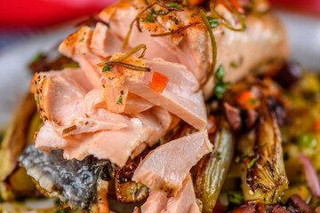 A seafood dinner serve of a piece of Salmon on top of grilled vegetables, in a round white plate