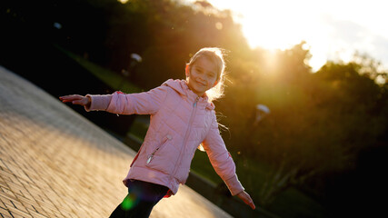 Fototapeta na wymiar Little cute backlit girl in pink jacket in a summer park