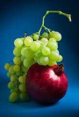 close-up, ripe red pomegranate and green grapes on a blue background