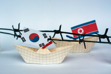 paper ship with Flags of North Korea and South Korea barbed wire between them. border conflict concept