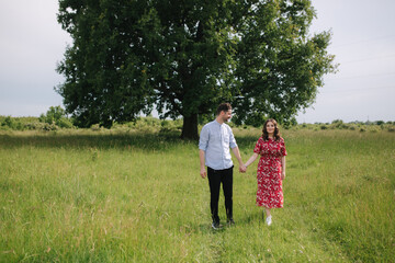 Young couple walking in front of big tree. Happpy man and woman spend time toghether. Woman in red dress