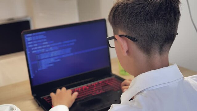 Portrait of child prodigy boy in glasses is programming the code at laptop at home. Young hacker works at a computer.